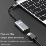Close-up van de adapter aangesloten op een laptop, met '4K UHD' tekst op de behuizing en een HDMI-kabel erin geplugd.