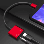 Rode vierkante USB-C naar 3.5mm jack adapter verbonden met telefoon en oplaadkabel