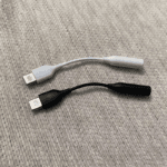 Realistische foto van de witte en zwarte USB-C naar 3.5mm adapters op een stoffen ondergrond