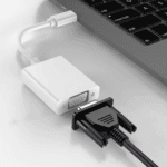 Close-up van een witte USB-C adapter aangesloten op de zijkant van een MacBook met VGA kabel